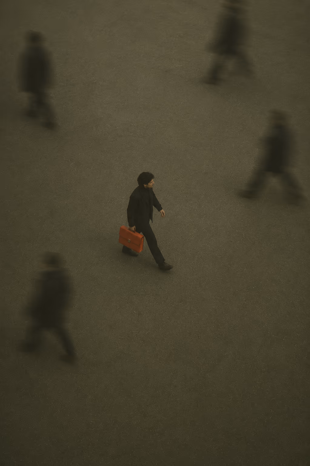 A person carrying a coral suitcase across a large shadowed plaza.